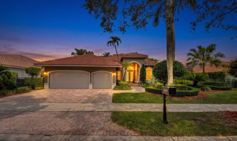 Twilight exterior of a single story South Florida home with barrel tile roof three car garage circular driveway and mature palm landscaping representative of the architecture inside Maple Island the gated sub community within The Islands of Weston FL where 1640 Island Way is hosting an open house Sunday May 24 2026